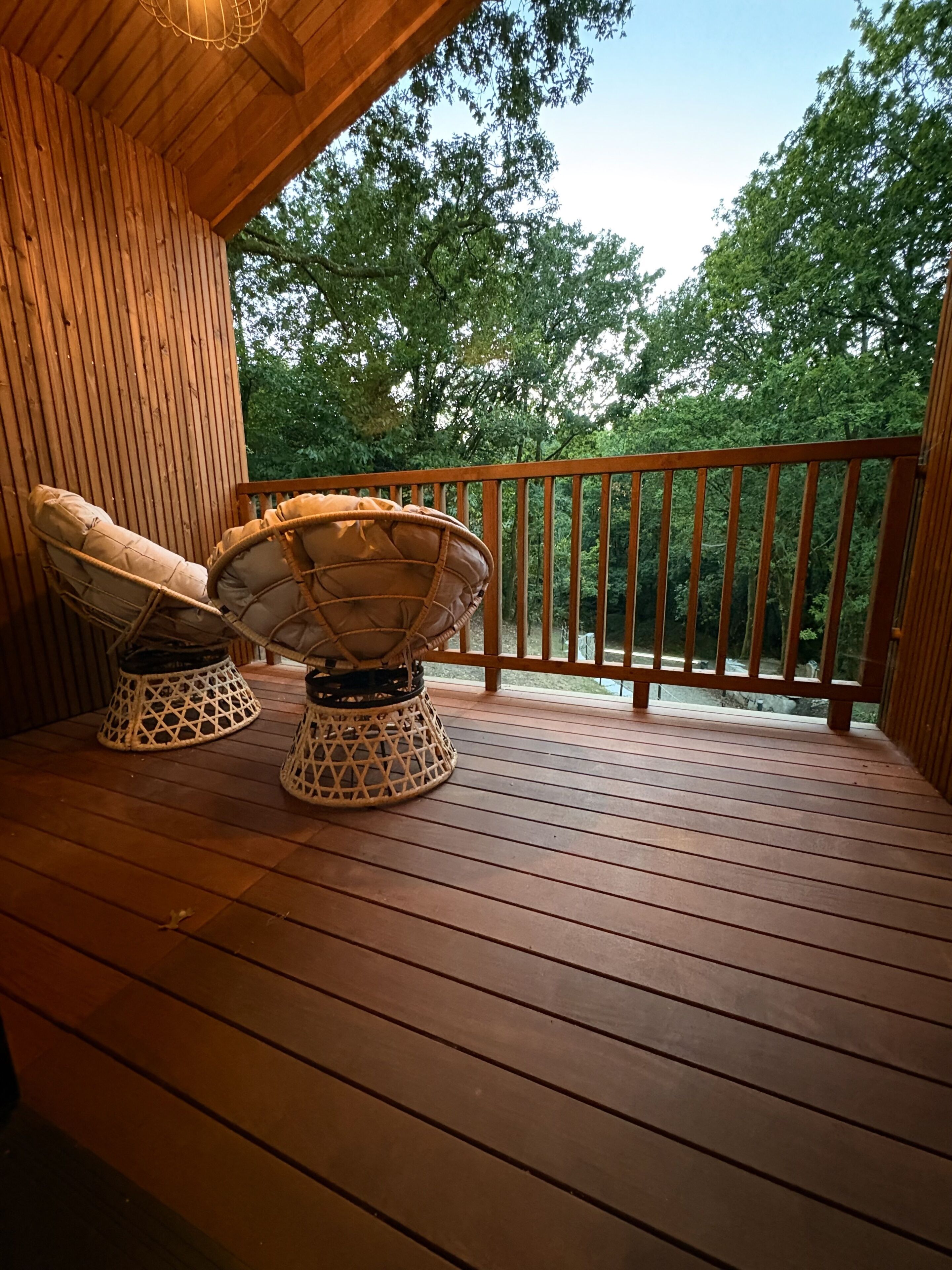 Une terrasse en bois avec deux chaises en osier et une rambarde.