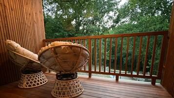 Une terrasse en bois avec deux chaises en osier et une rambarde.