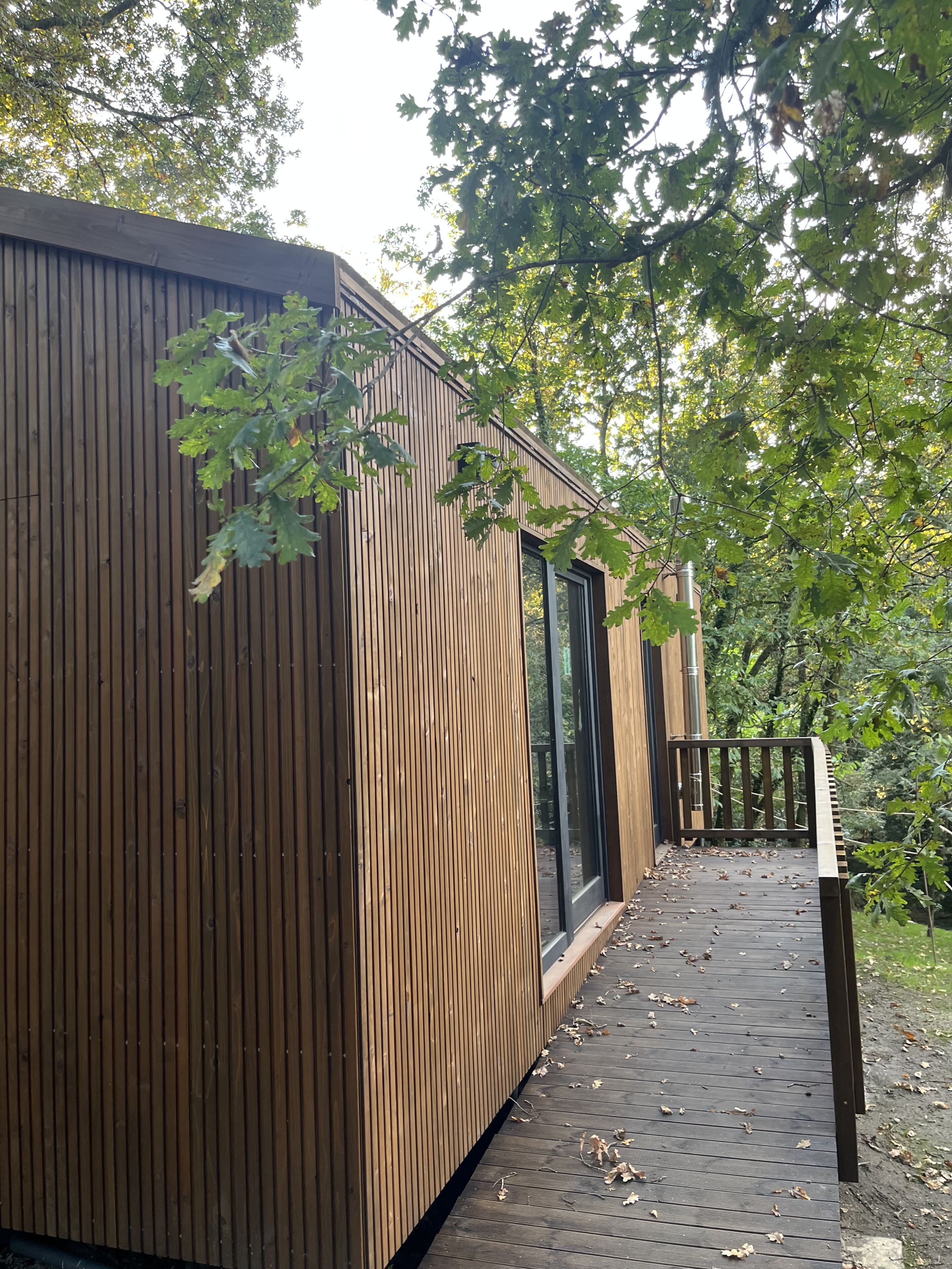 A wooden cabin with a deck, large windows, and a view of the surrounding trees.