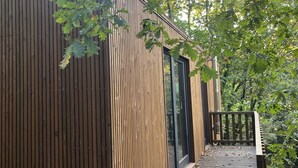 A wooden cabin with a deck, large windows, and a view of the surrounding trees. - Refuxio da Carballeira - Cabin 1 (pet-friendly) (Rebordelo (San Martiño))