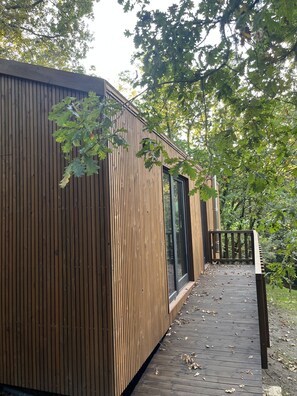 Uma cabana de madeira com varanda, grandes janelas e vista para as árvores ao redor.