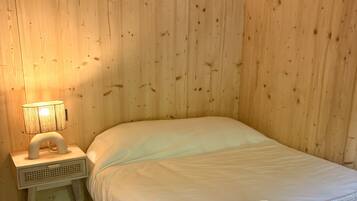 Habitación con paneles de madera, una cama, una mesita de noche con lámpara y toallas enrolladas sobre la cama.