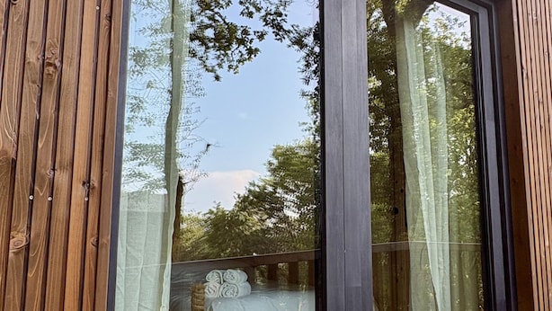 A modern room with a large window, wooden walls, and a bed with a white bedspread and rolled towels. - Refuxio da Carballeira - Cabin 1 (pet-friendly) (Rebordelo (San Martiño))