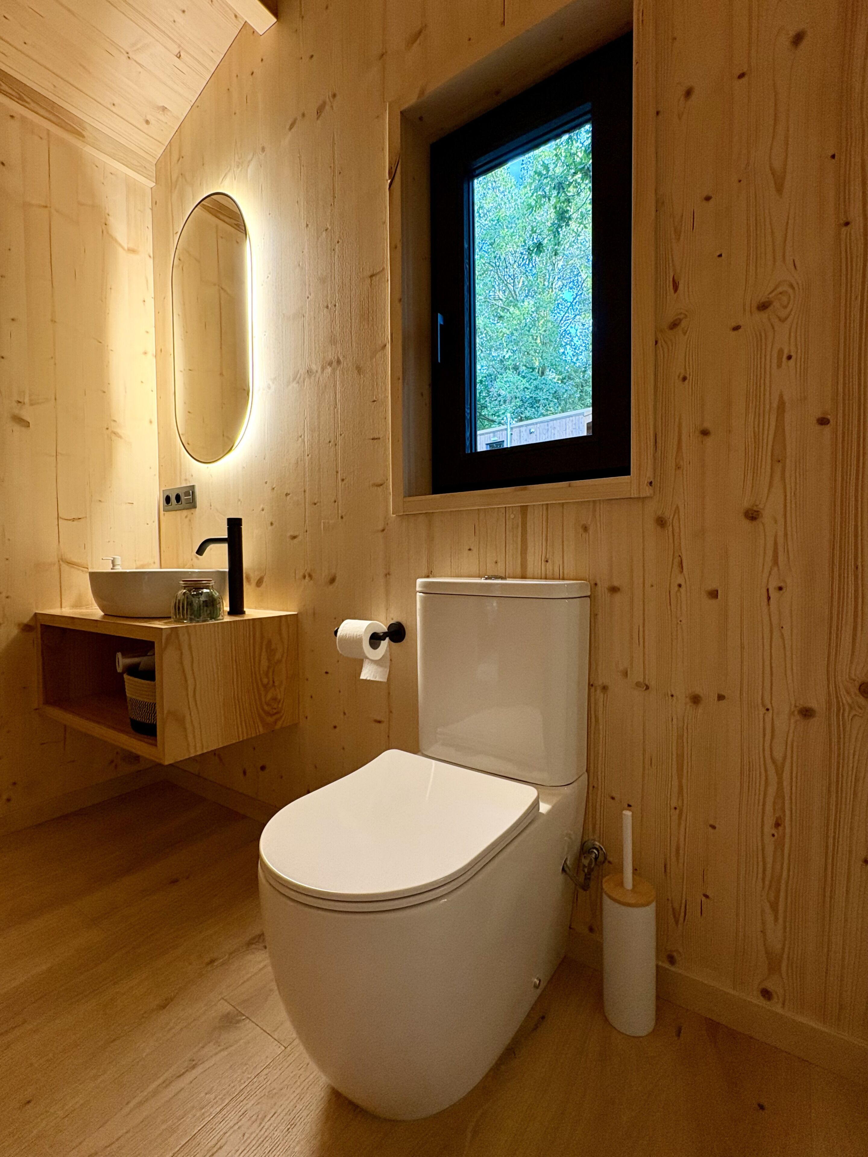 Un baño de madera con inodoro, lavamanos y ventana.