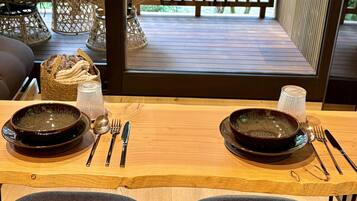 Mesa lista con platos, cubiertos y una cesta de pan, con vista a una terraza de madera con mobiliario exterior.