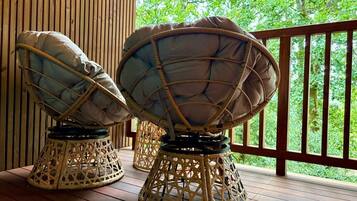 Twee rieten stoelen met kussens op een houten terras, met uitzicht op groen.