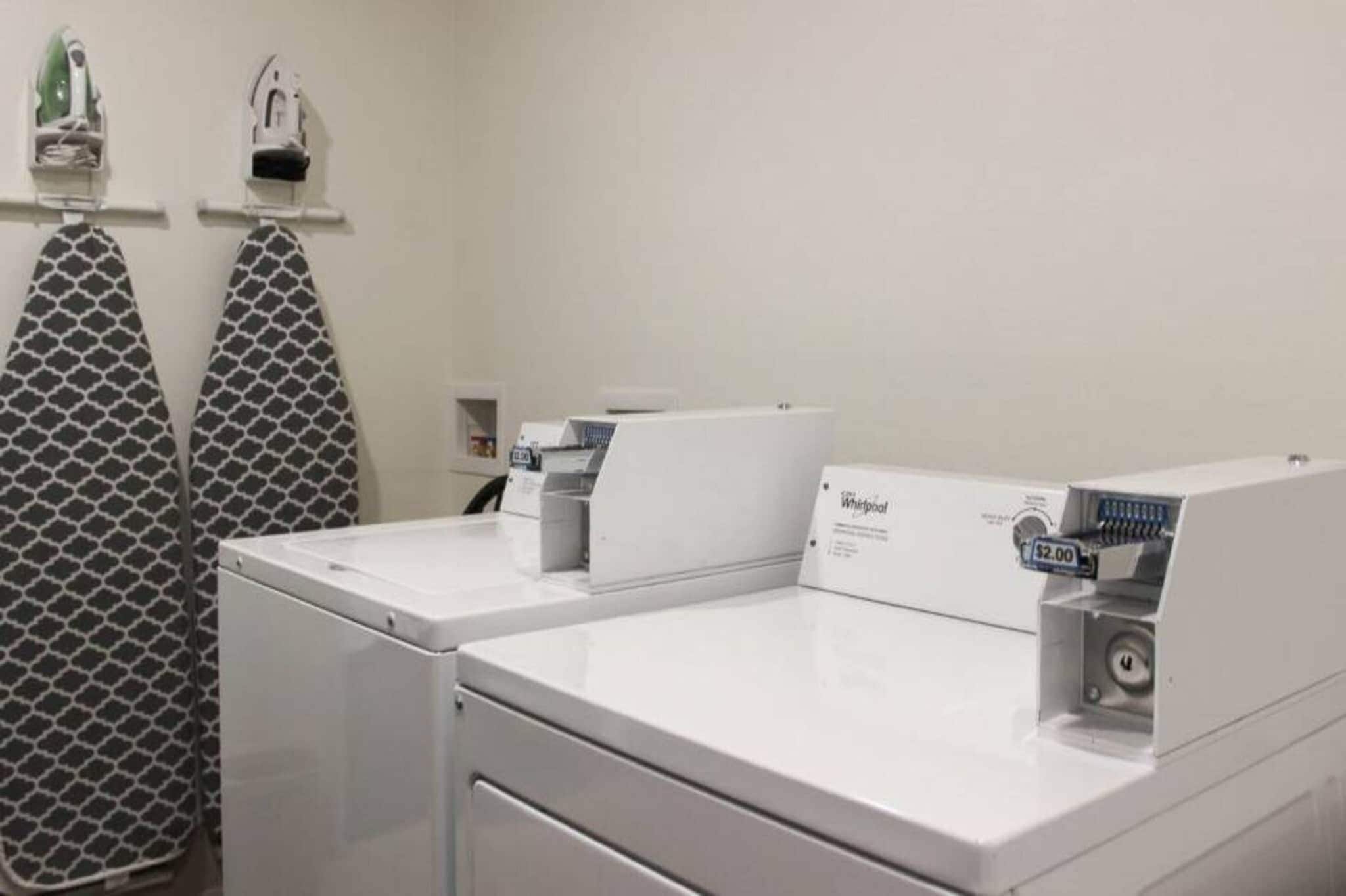 A laundry area with two Whirlpool washers, a patterned towel rack, and a small shelf with items.
