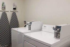 A laundry area with two Whirlpool washers, a patterned towel rack, and a small shelf with items.