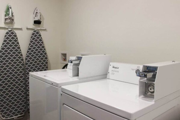 A laundry area with two Whirlpool washers, a patterned towel rack, and a small shelf with items.