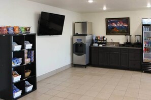 A clean, well-lit room with a flat-screen TV mounted on the wall, a refrigerator, a water dispenser, and a coffee machine on the counter.