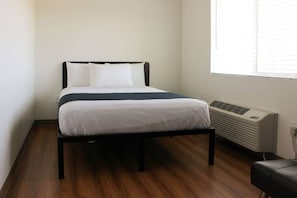 A single bed with a dark frame, white bedding, and a window with blinds to the right. - 1 Queen Bed | Non-Smoking (Rexburg)