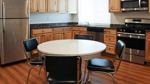 Eine Küche mit einem runden Tisch, vier Stühlen, einem Kühlschrank, einer Mikrowelle, einem Backofen und Holzschränken.