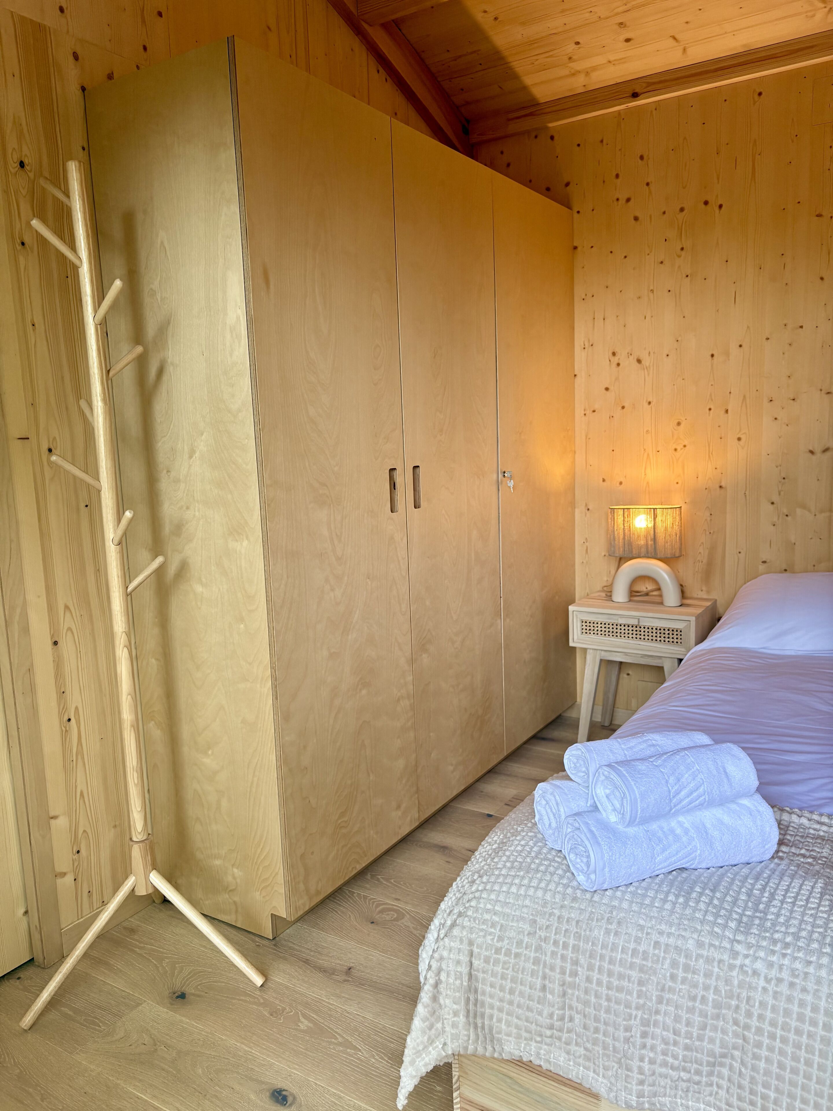 Een houten kamer met een bed, nachtkastje en garderobe.