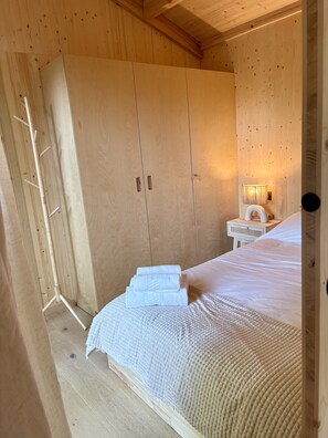 Quarto de madeira com uma cama, um guarda-roupa e uma mesa de cabeceira com abajur.