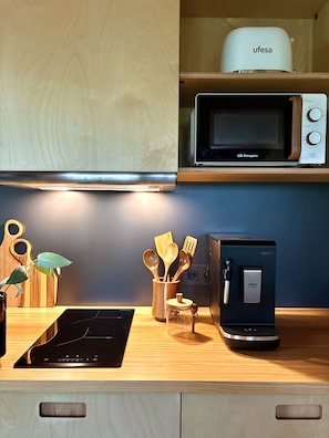 Una cocina con microondas, cafetera, utensilios de madera y una planta.
