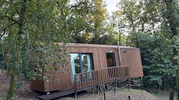 Una pequeña cabaña de madera con puerta de cristal, rodeada de árboles.