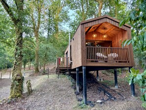 Een houten boomhut met een balkon, omringd door een bos.