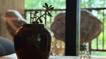 Un vase en céramique de couleur sombre, orné d’une plante, est posé sur une table en bois près d’une fenêtre donnant sur un paysage verdoyant.