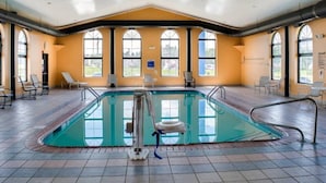 Una piscina interior con paredes de vidrio transparente, varias ventanas y sillones de descanso.