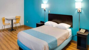 Una habitación de hotel con una cama, dos mesitas de noche, una silla, una pequeña mesa y una lámpara.
