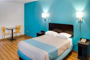 A hotel room with a bed, two bedside tables, a chair, a small table, and a lamp. - 1 KING BED | SUITE, NON-SMOKING, HOT TUB (Richmond IN)