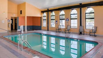 An indoor swimming pool with clear water, surrounded by windows and chairs.