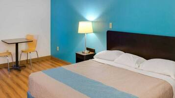 Una habitación de hotel con cama, escritorio, silla y mesita de noche con lámpara.