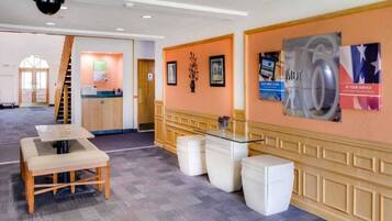 A hotel lobby with a reception desk, a staircase, and a seating area with a table and chairs.