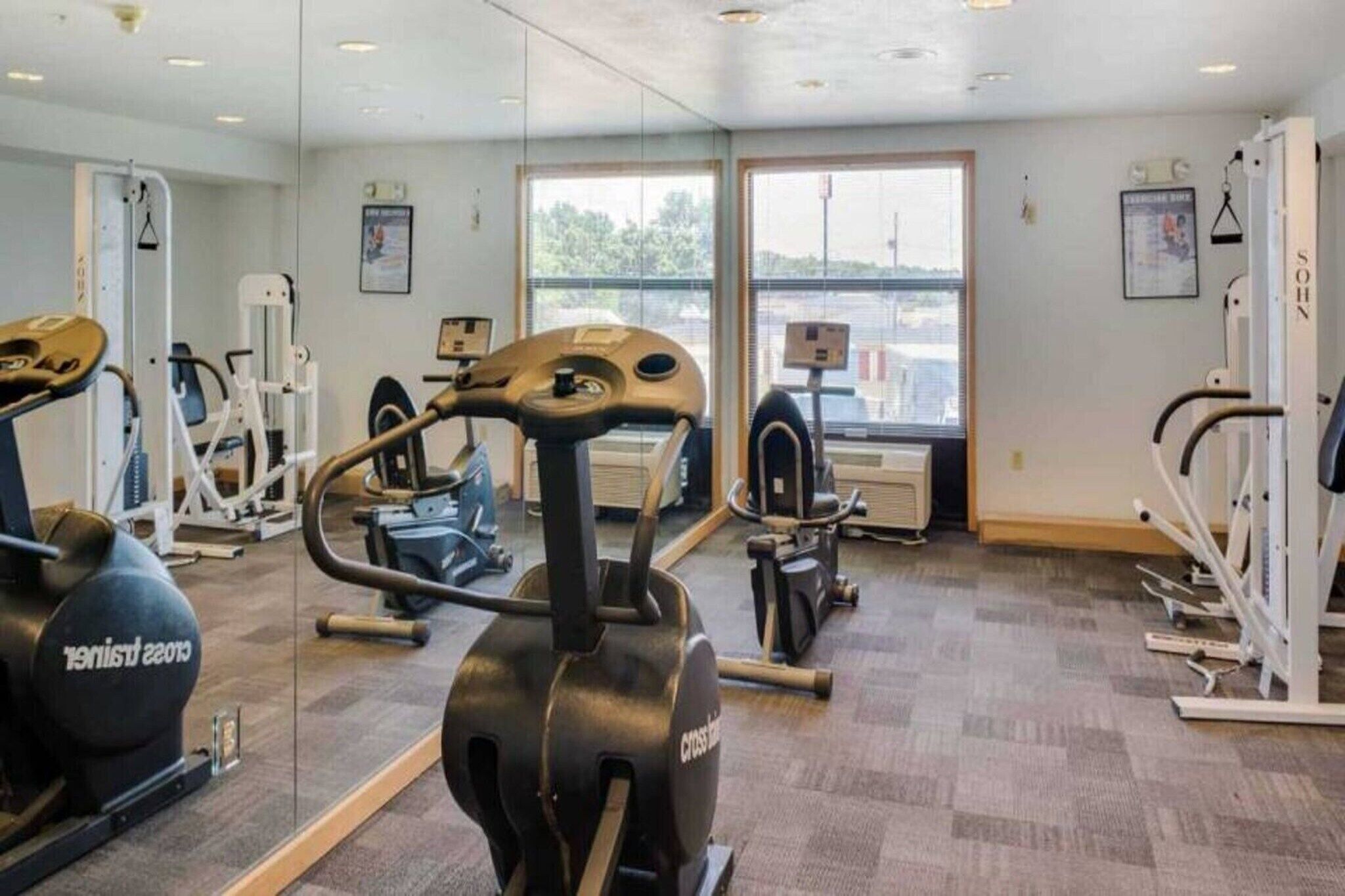 Un gimnasio con diversos equipos de ejercicio, amplias ventanas y vistas al exterior.