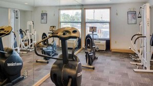 Un gimnasio con diversos equipos de ejercicio, amplias ventanas y vistas al exterior.