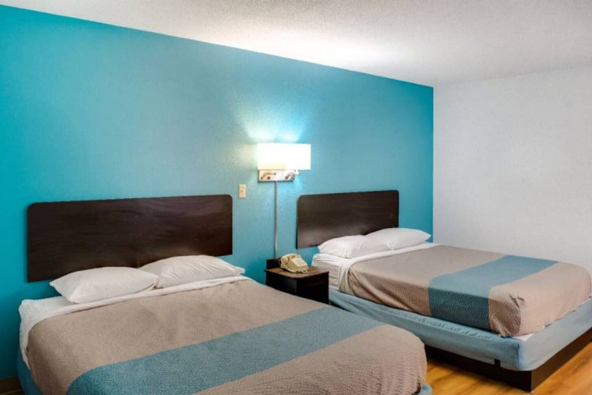 A hotel room with two beds, a nightstand with a lamp, and a wall-mounted telephone.