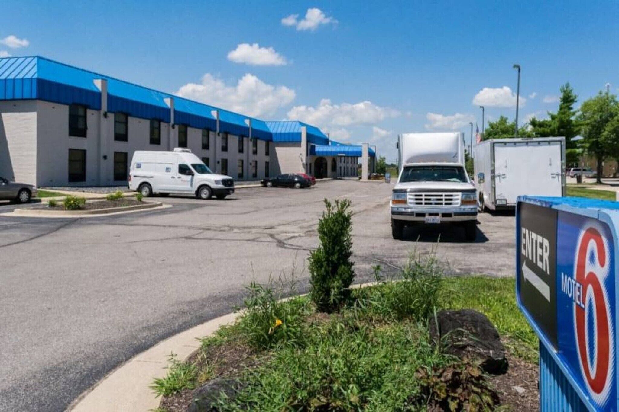 A motel with a blue roof, a parking lot with several vehicles, and a sign indicating the motel's name.