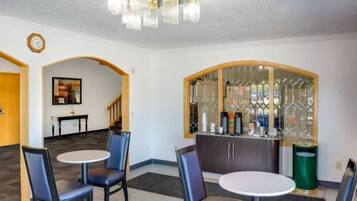 A dining area with two round tables and chairs, a bar area with a glass partition, and a clock on the wall.