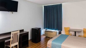 A hotel room with a bed, a desk, a chair, a TV, and a window with curtains.