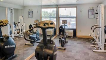 Ett gym med konditionsmaskiner, styrketräningsmaskiner och ett stort fönster som släpper in naturligt ljus.