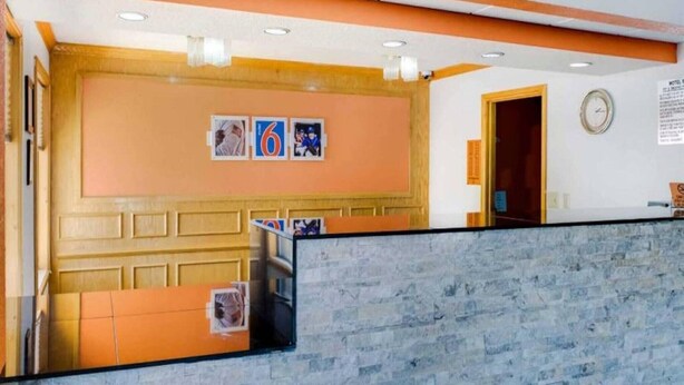 Zona de recepció amb taulell d'informació, un rellotge i una paret amb dos quadres emmarcats.