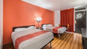 A hotel room with two beds, a desk, a chair, and a door.