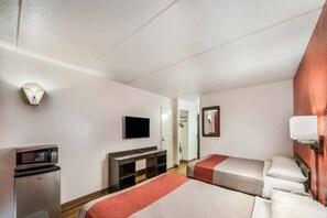 A hotel room with a bed, a desk with a microwave, a television, and a mirror. - 2 Queen Beds | Non-Smoking, Micfridge (HENDERSON)