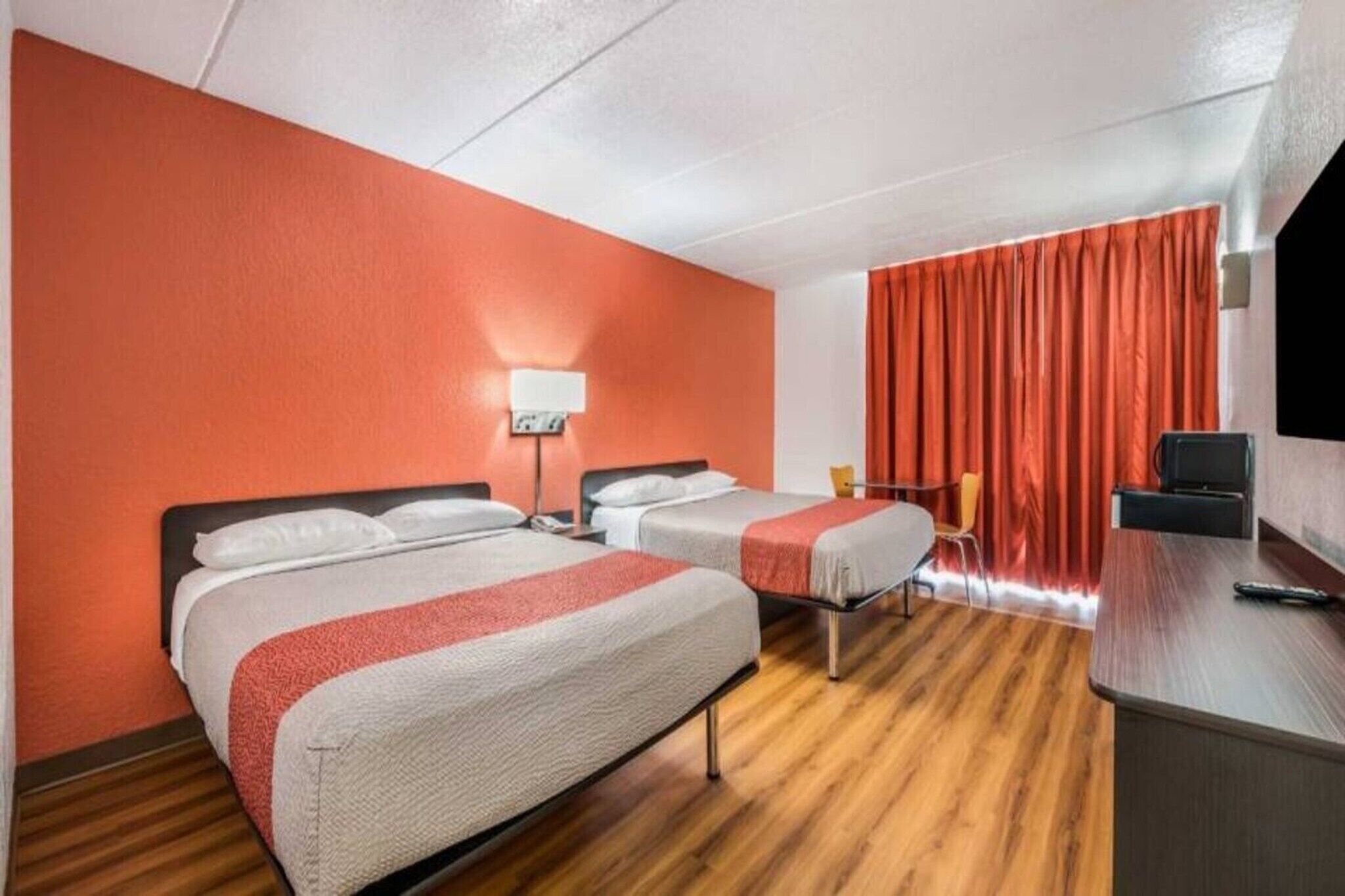 Habitación de hotel con dos camas, un escritorio, una silla, un televisor y una cortina roja.