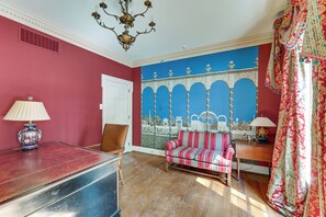 Una habitación con una pared roja, un sofá estampado, una araña y un mural de un paisaje urbano.