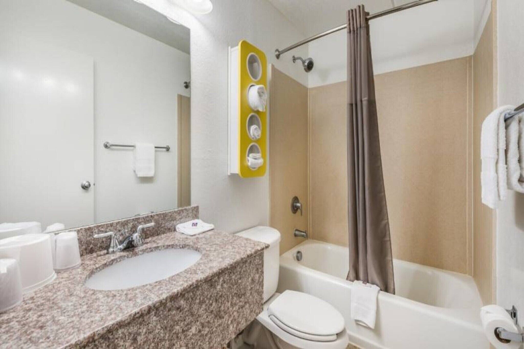 Une salle de bain avec un lavabo sur un plan de travail en granit, des toilettes, une baignoire et un rideau de douche.