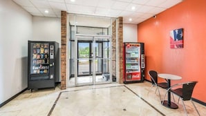 Et lobbyområde med en automat, en glasdør og et siddeområde med et bord og stole.