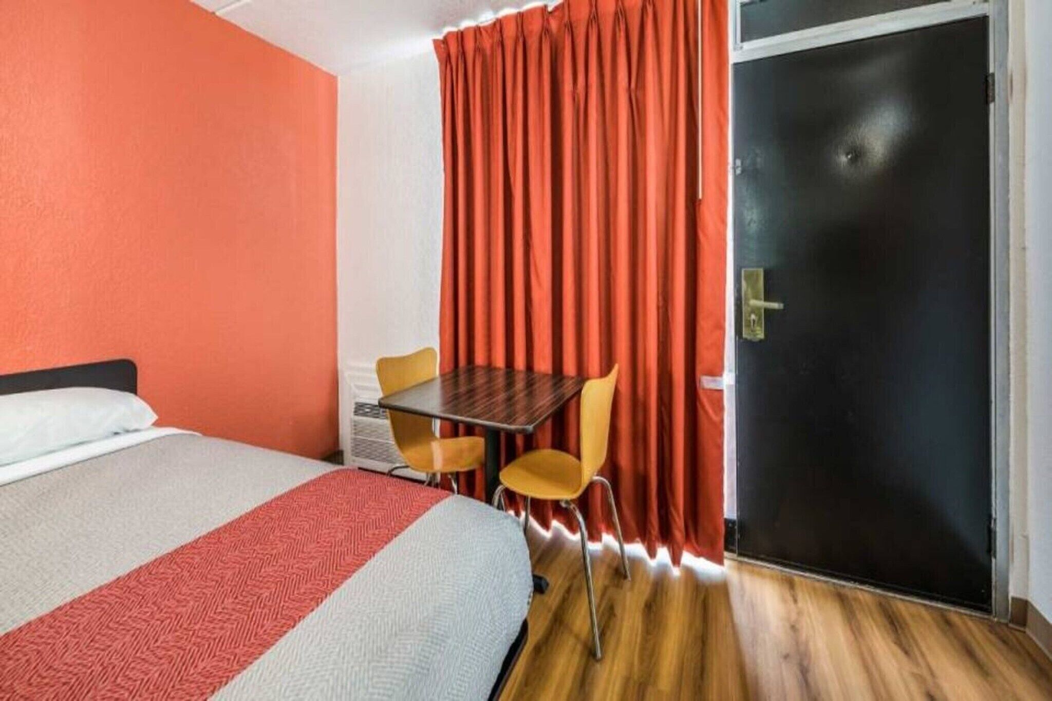 A hotel room with a bed, a table, two chairs, a door, and a curtain.