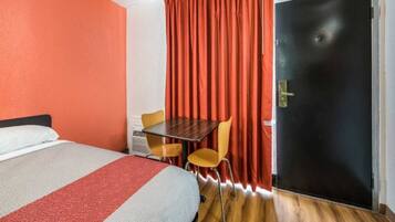 A hotel room with a bed, a table, two chairs, a door, and a curtain.