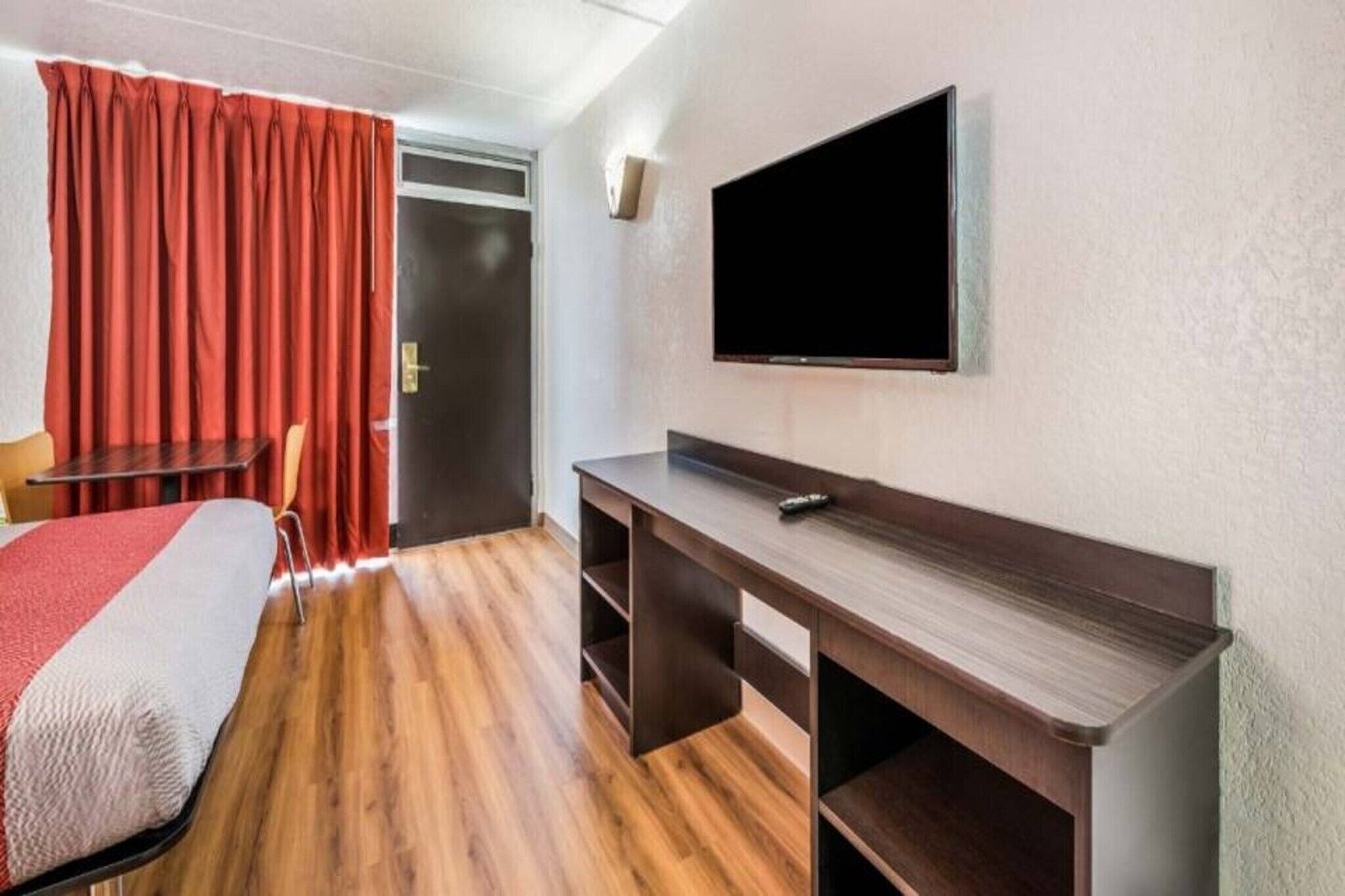 Habitación de hotel con cama, escritorio, televisor y puerta.