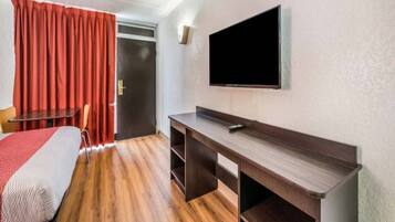 Habitación de hotel con cama, escritorio, televisor y puerta.