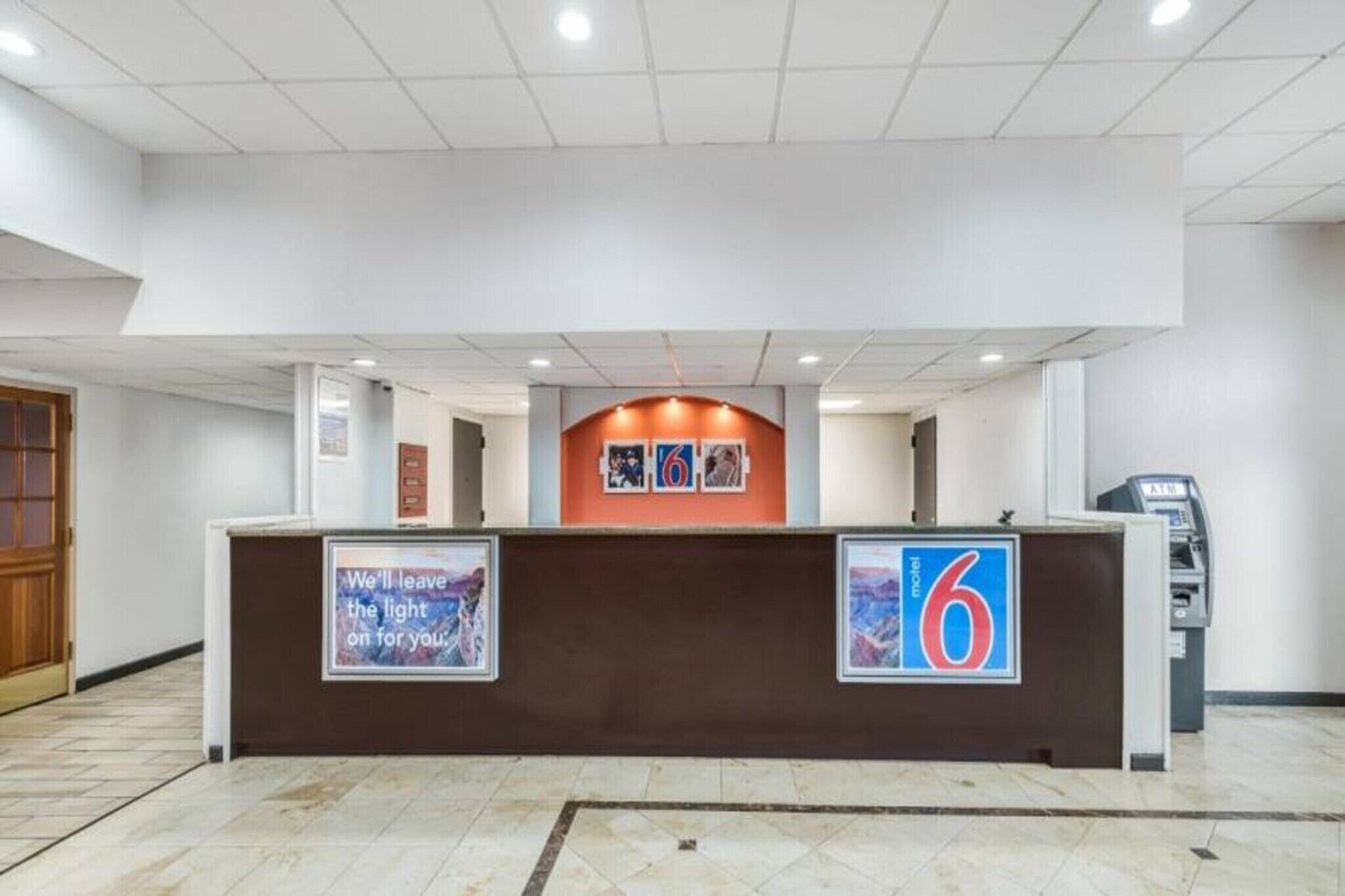 A hotel reception desk with a number 6 sign, a framed quote, and an ATM machine.