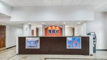 A hotel reception desk with a number 6 sign, a framed quote, and an ATM machine.