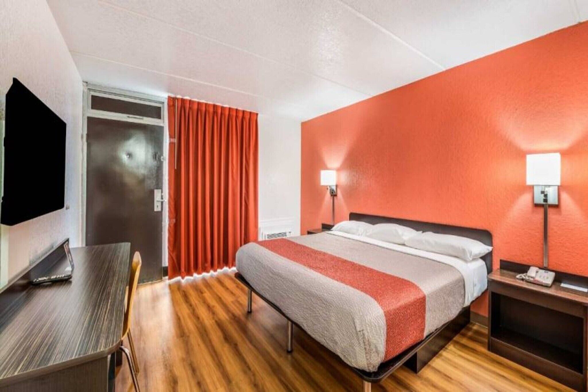 Una habitación de hotel con cama, mesita de noche, lámpara, televisor y escritorio con silla.