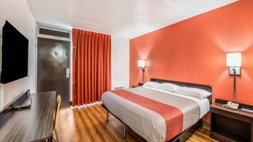 Una habitación de hotel con cama, mesita de noche, lámpara, televisor y escritorio con silla.